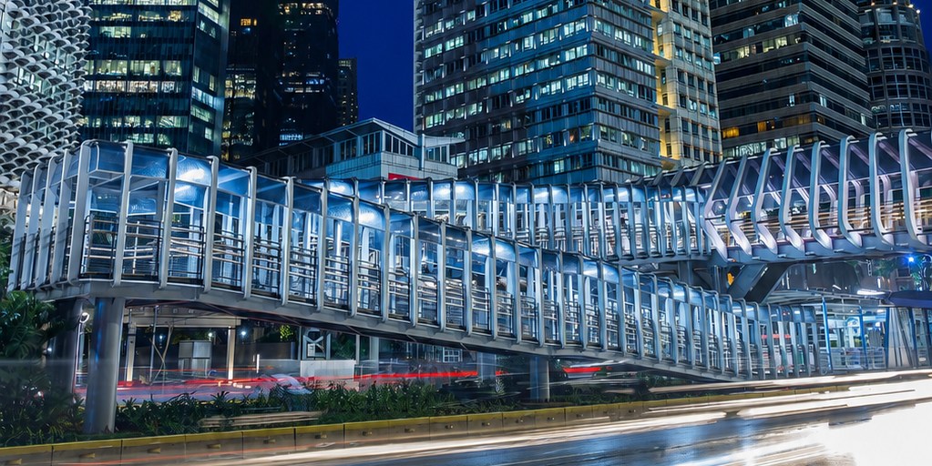 Illuminated polycarbonate-glazed pedestrian skybridge among city towers at night